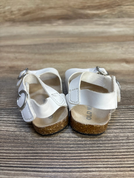 White toddler sandals with cork soles and buckles on a wooden surface