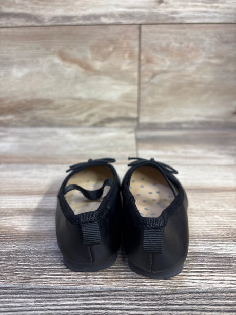 Rear view of Cat and Jack toddler black slip-on ballet flats showing elastic heel loop, bow accent, and polka-dot insole on wood floor