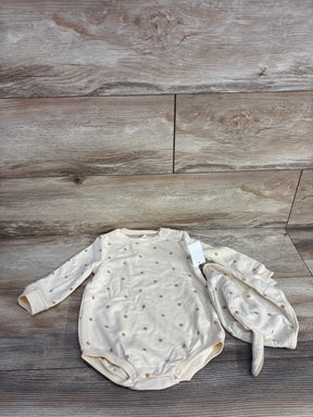 Cream-colored long-sleeve baby onesie with tan polka dots and matching hat on wood floor