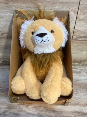 Plush lion stuffed animal with white mane sitting in a cardboard box on wooden floor