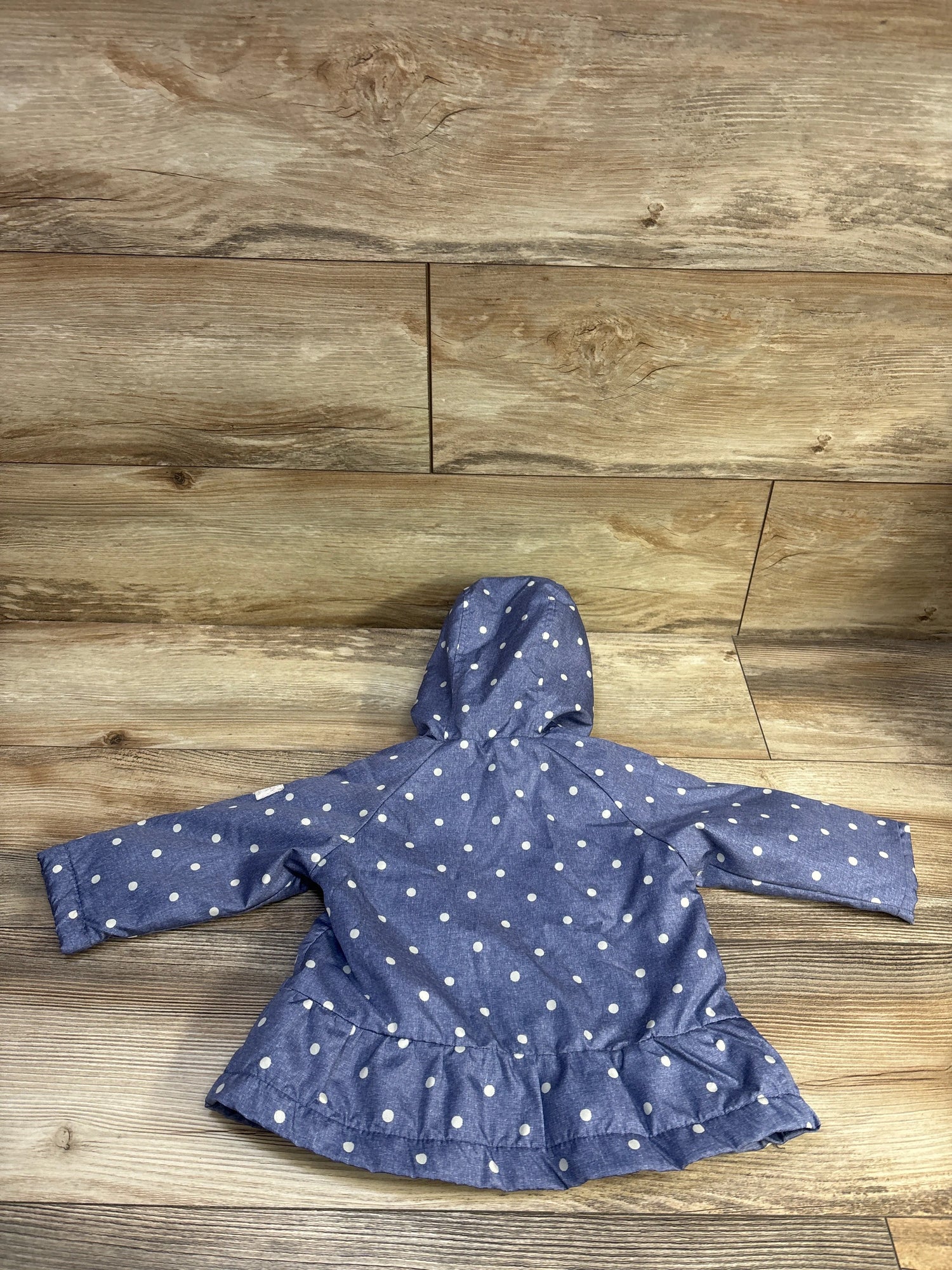 Back view of Oshkosh blue polka dot hooded jacket showcasing long sleeves and ruffled hem on a wood floor