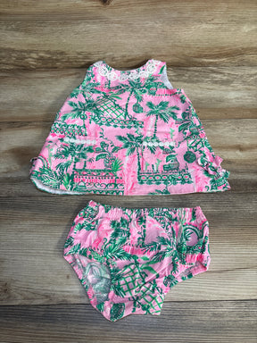 Pink and green tropical baby dress and bloomers set with lace trim on a wood background.