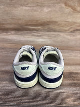 Rear view of Nike Dunk Low TD sneakers showing NIKE heel tabs in midnight navy and volt tint on wood floor
