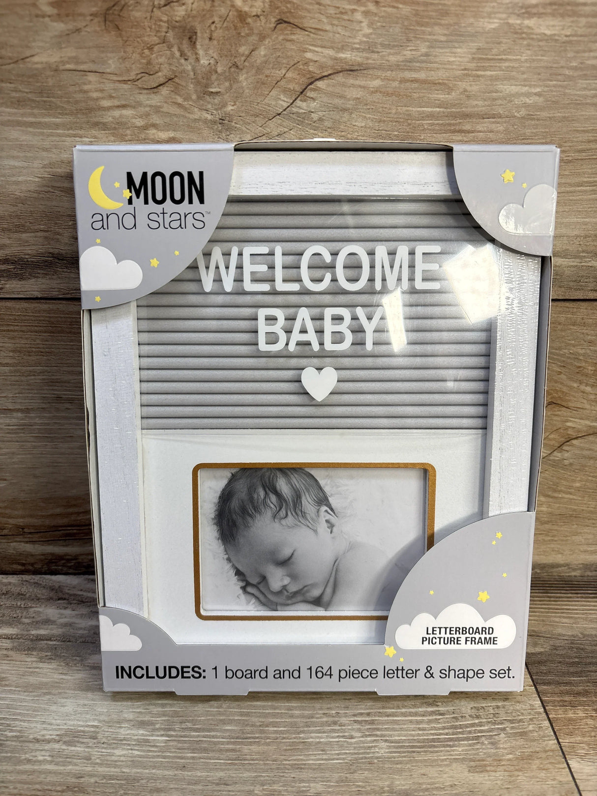 Front view of Moon and Stars letterboard frame in box showing WELCOME BABY, heart and photo slot on wood background