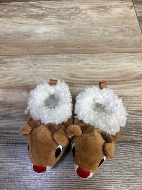 Top view of brown Rudolph the Red-Nosed Reindeer plush slippers showcasing white furry cuffs and red noses on wood-look flooring