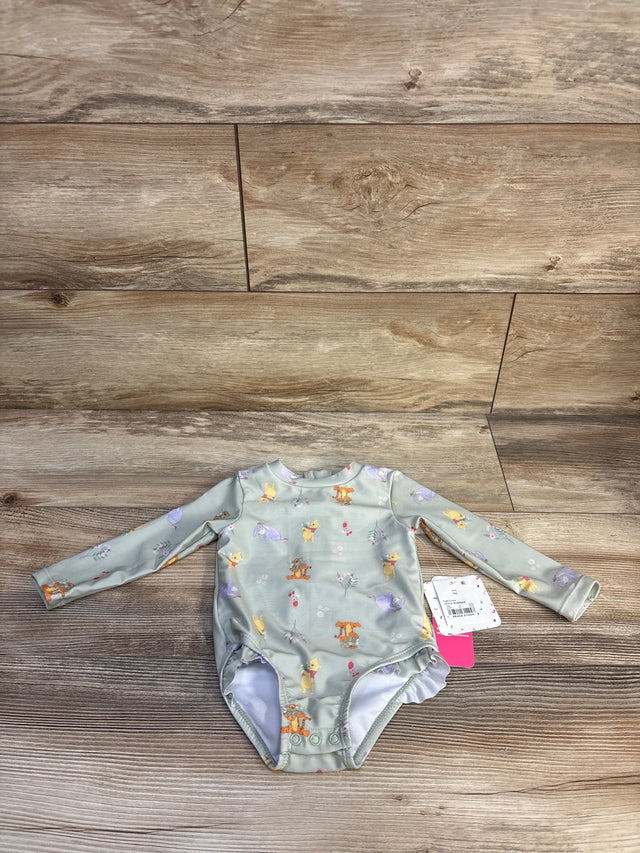 Flat lay of Disney Baby Winnie the Pooh long sleeve rash guard one piece in sage with character print and hangtag on wood plank floor