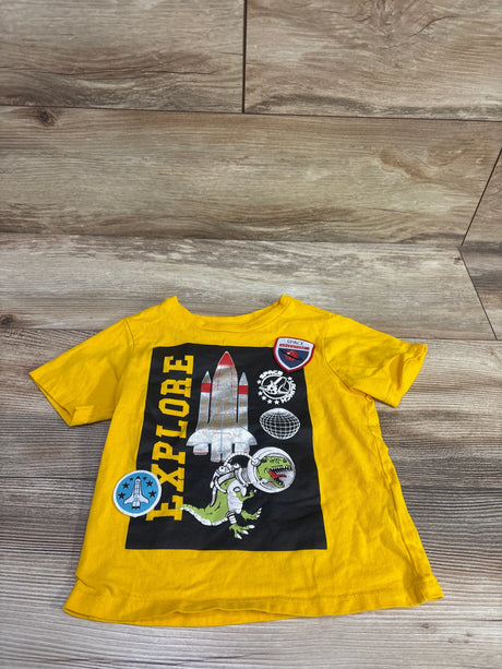 Front view of yellow Maximus Rex space shirt in size 2T showcasing a rocket, astronaut dinosaur, globe, and Explore graphic on a wood background