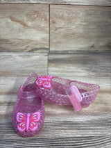 Front and side view of toddler pink glitter jelly Mary Jane flats showcasing butterfly charm and Velcro strap on wood background