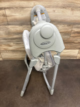 Rear three-quarter view of Graco Slim Spaces compact baby swing showcasing folded frame and Graco logo against wood-paneled wall and brown floor