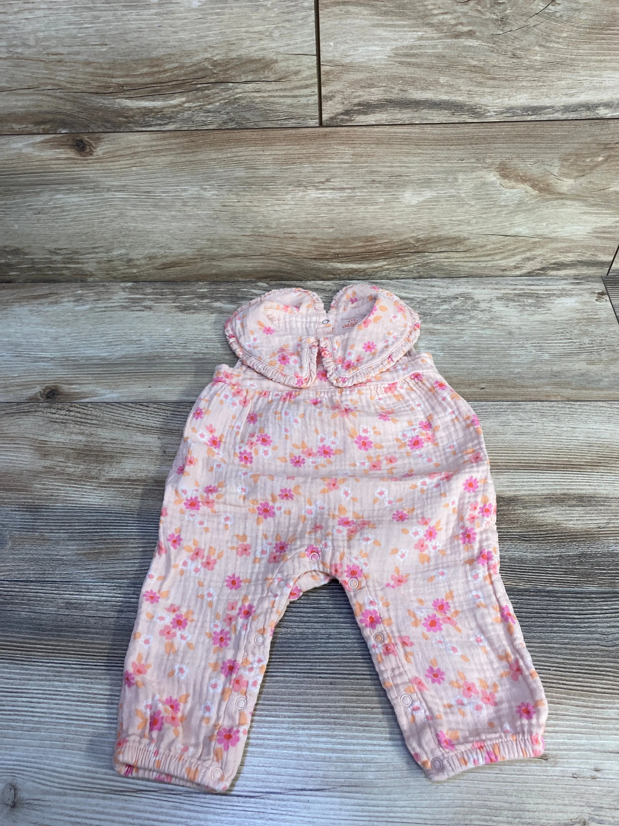 Flat lay of Cat & Jack pink collared gauze baby jumpsuit showing floral print and snap closures on light wood background