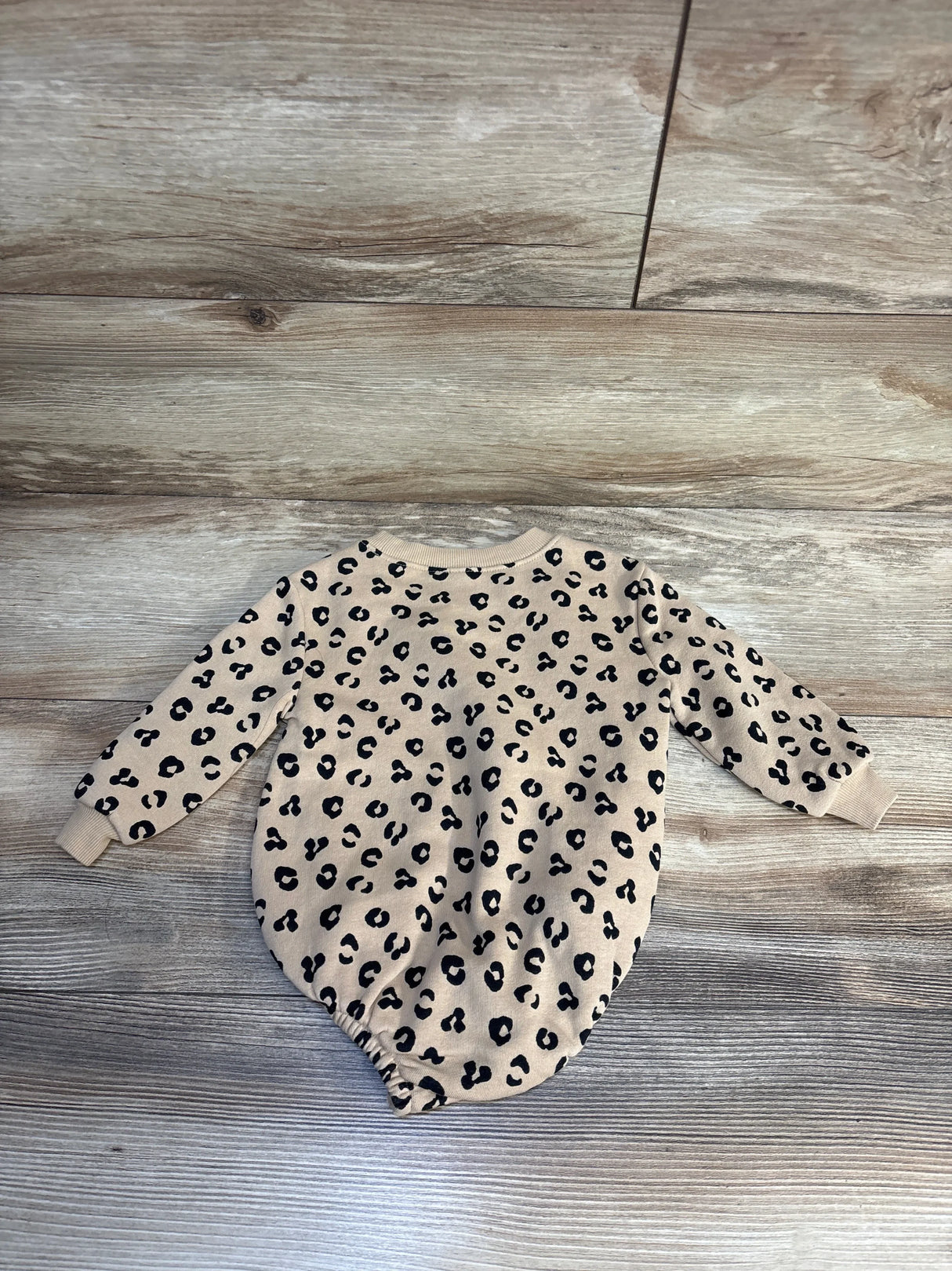 Beige baby onesie with black leopard print, long sleeves, laid on wood floor