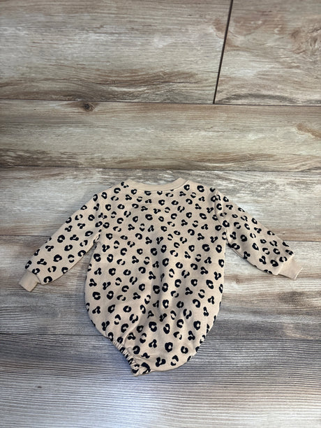 Beige baby onesie with black leopard print, long sleeves, laid on wood floor
