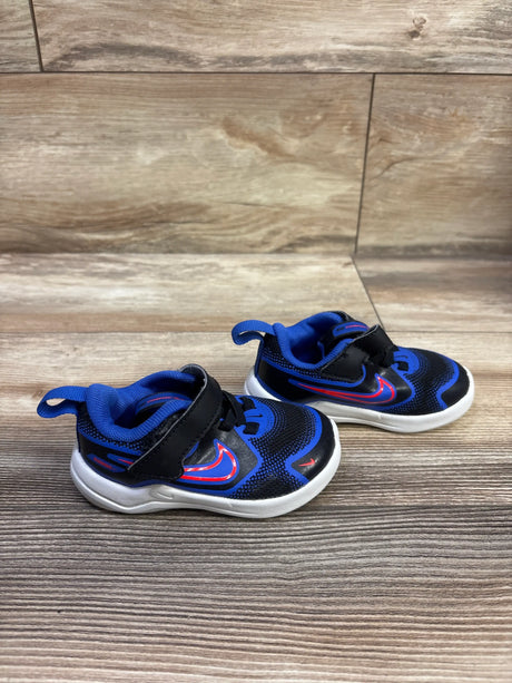 Angled view of Nike Cosmic Runner TD black and blue size 5C sneakers with hook-and-loop straps and white soles on a wood surface