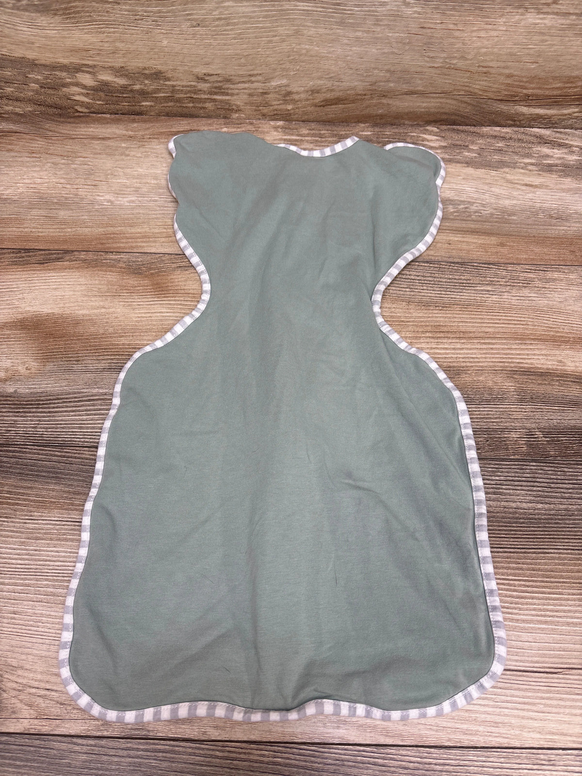 Flat lay of Love To Dream Swaddle Up Lite swaddle in green, size small/newborn, showcasing striped trim on a wood background