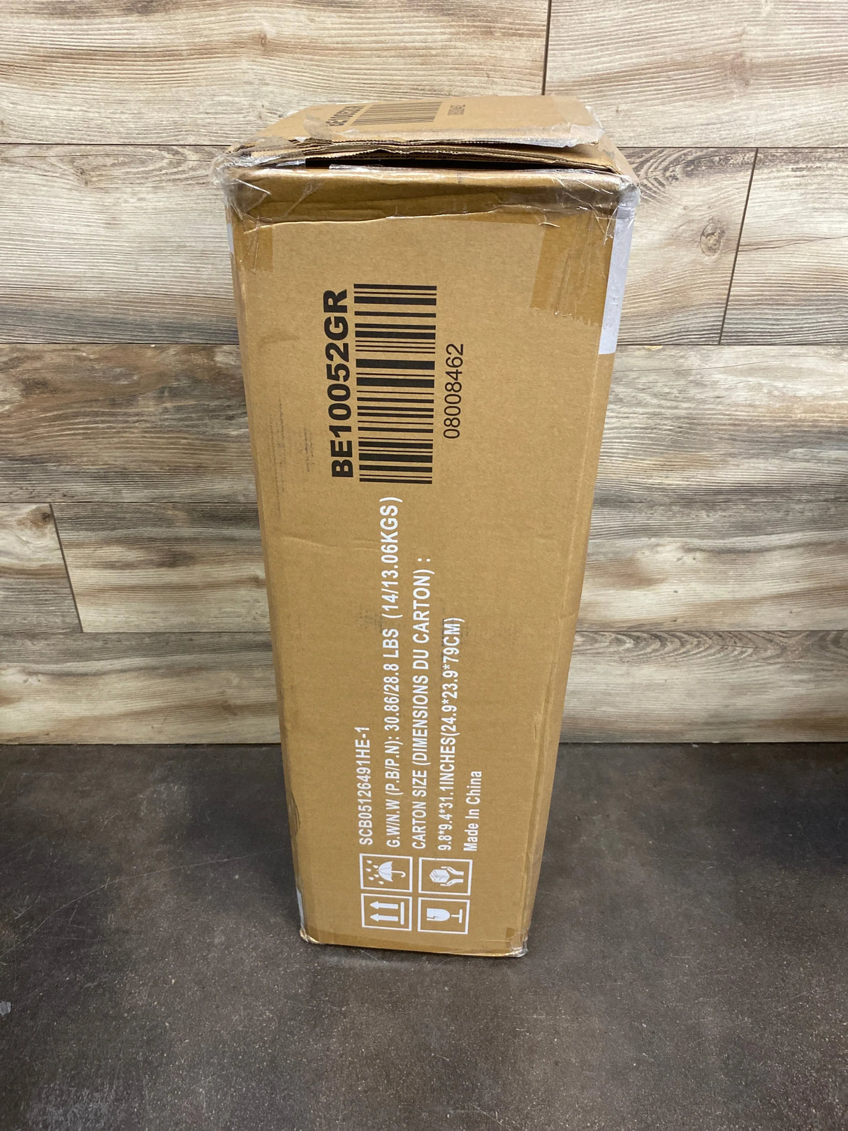 Brown cardboard box with shipping labels and barcode, placed on wooden floor