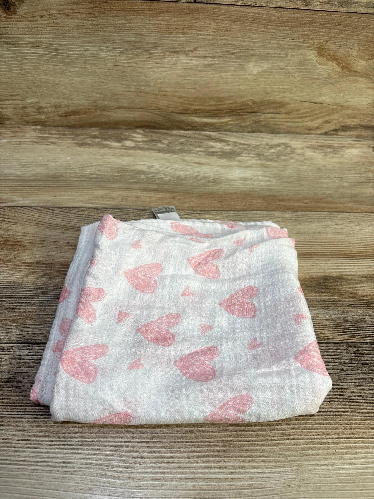 Folded view of GLLQUEN muslin bamboo swaddle blanket showcasing pink heart pattern on white fabric with wood background