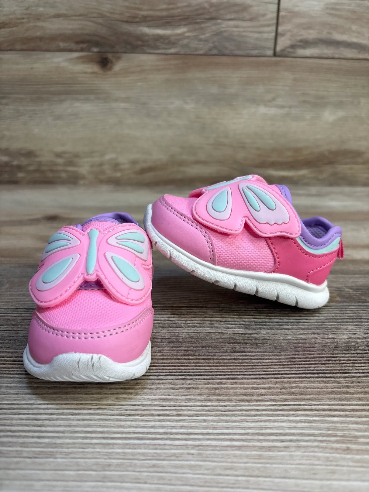 Pink toddler shoes with butterfly wings, white soles, on wood background