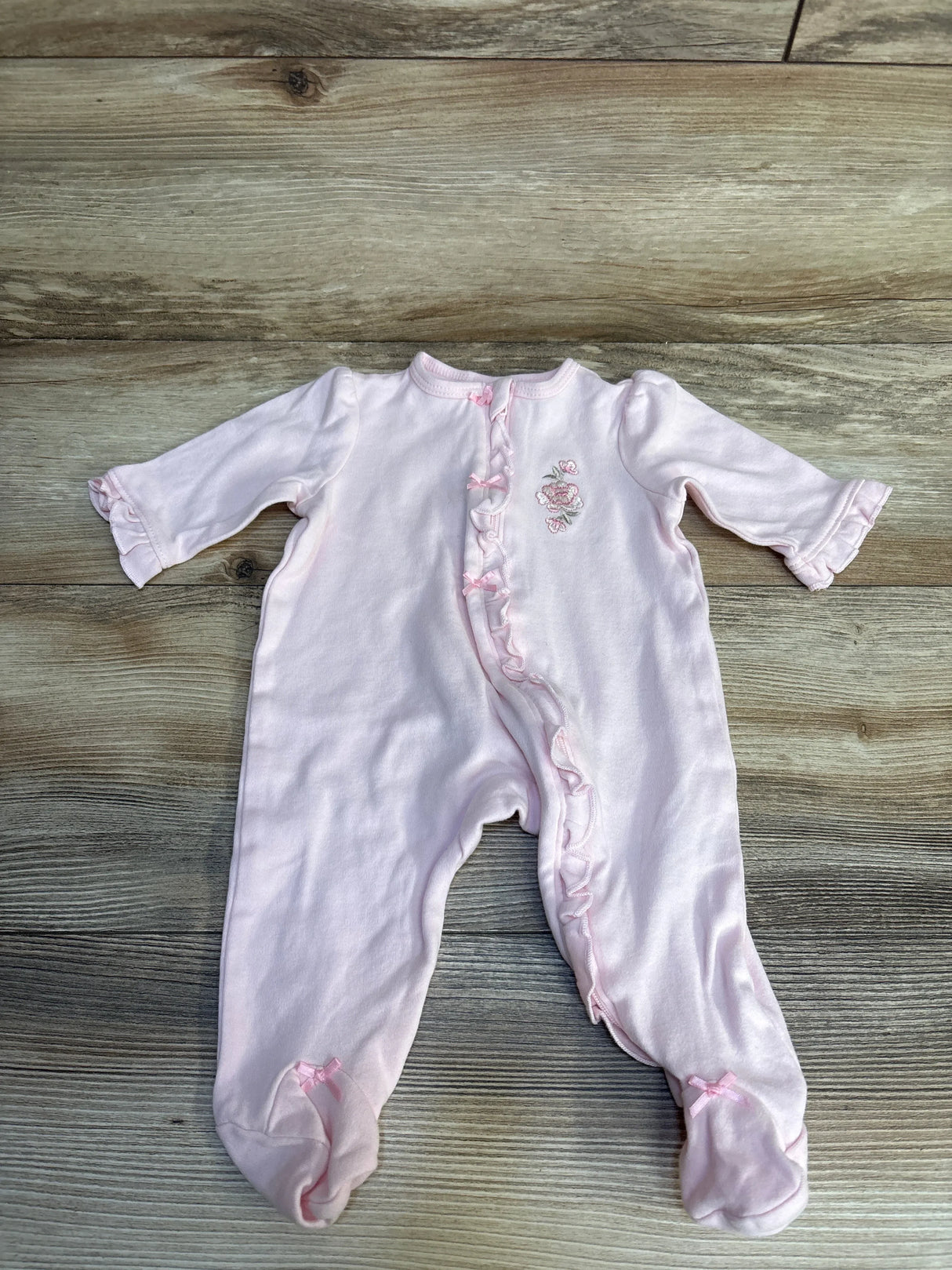 Pink baby onesie with floral embroidery and ruffled details on wooden floor