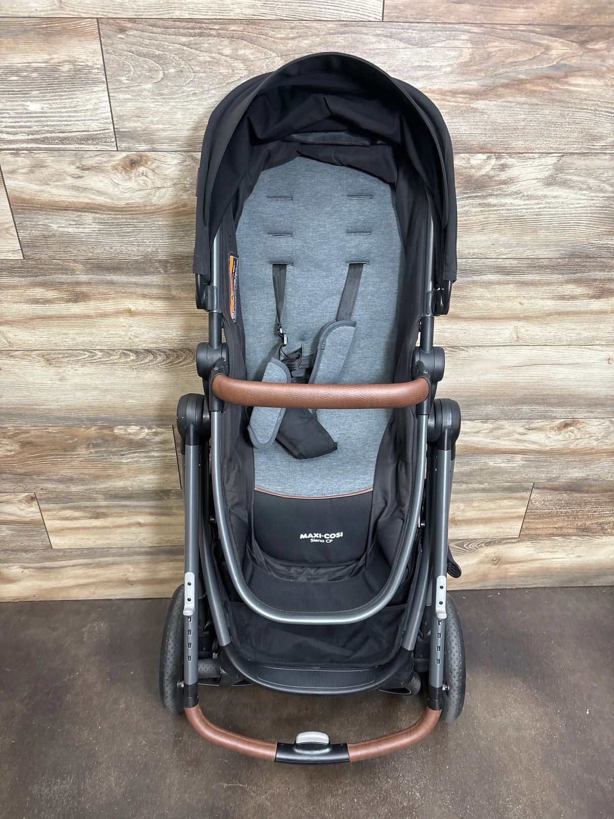 Maxi-Cosi black and gray baby stroller with brown handlebar, wooden floor background