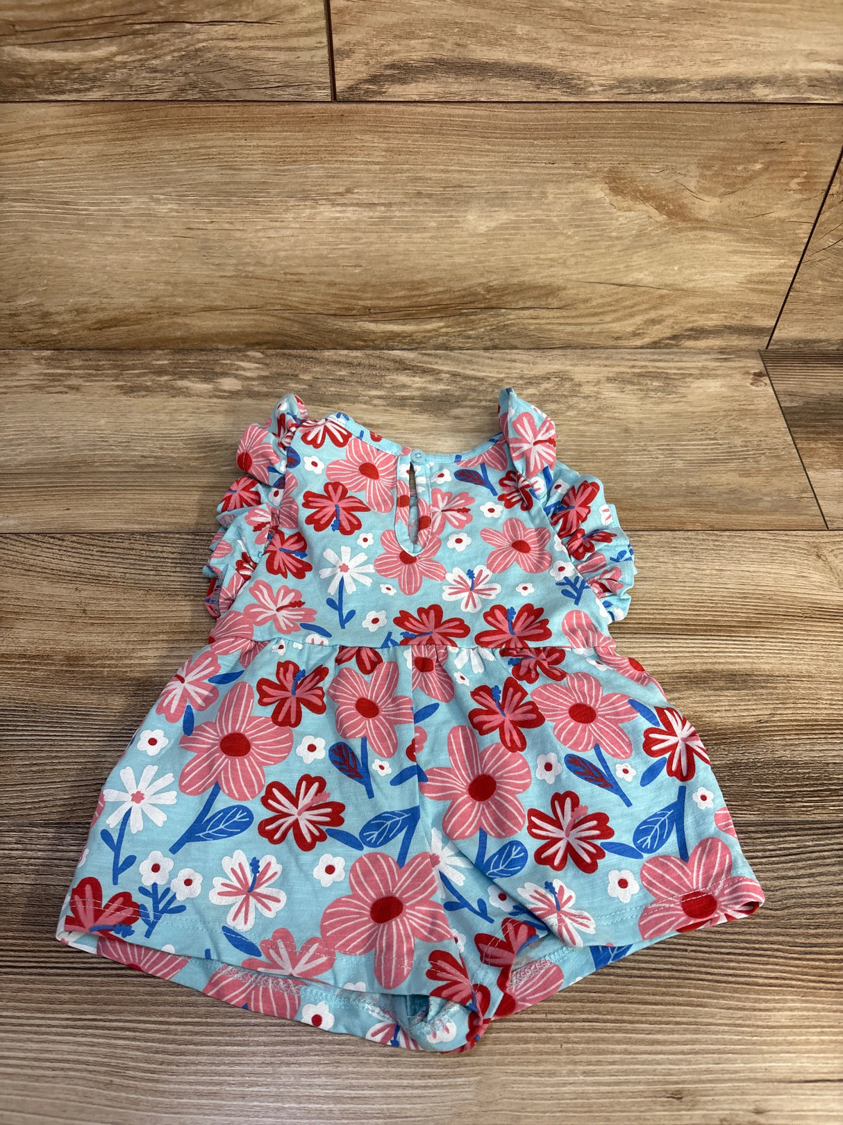 Flat lay of light blue shortie romper showcasing ruffle sleeves and pink and red floral print on wooden floor background
