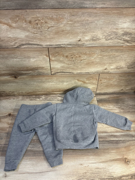 Top-down view of grey Champion 2-piece toddler hoodie and joggers, back of hooded pullover showing small dark stain, on wood floor, size 18 months