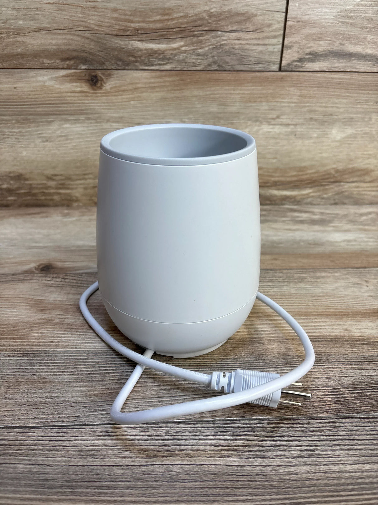White electric baby bottle warmer on wooden surface with power cord