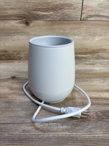 White electric baby bottle warmer on wooden surface with power cord
