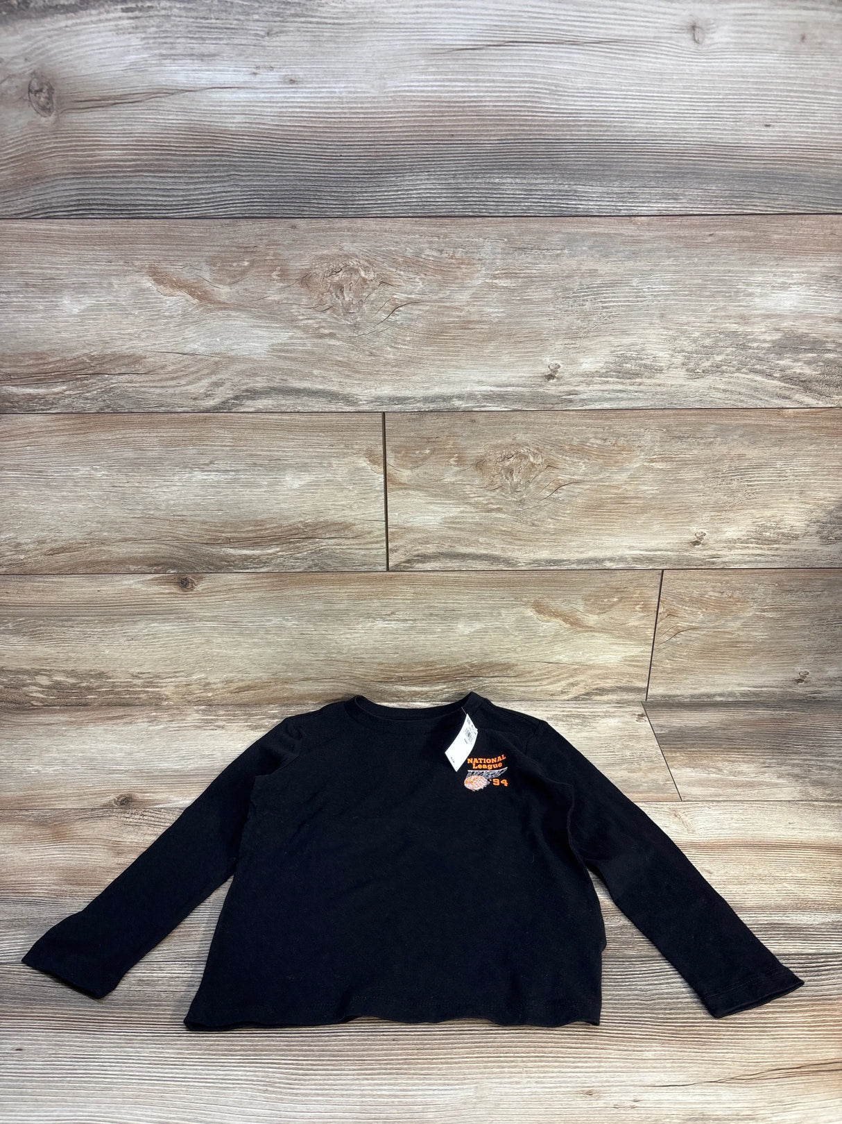 Black kids long sleeve shirt with National League '94 graphic, laid flat on wood floor