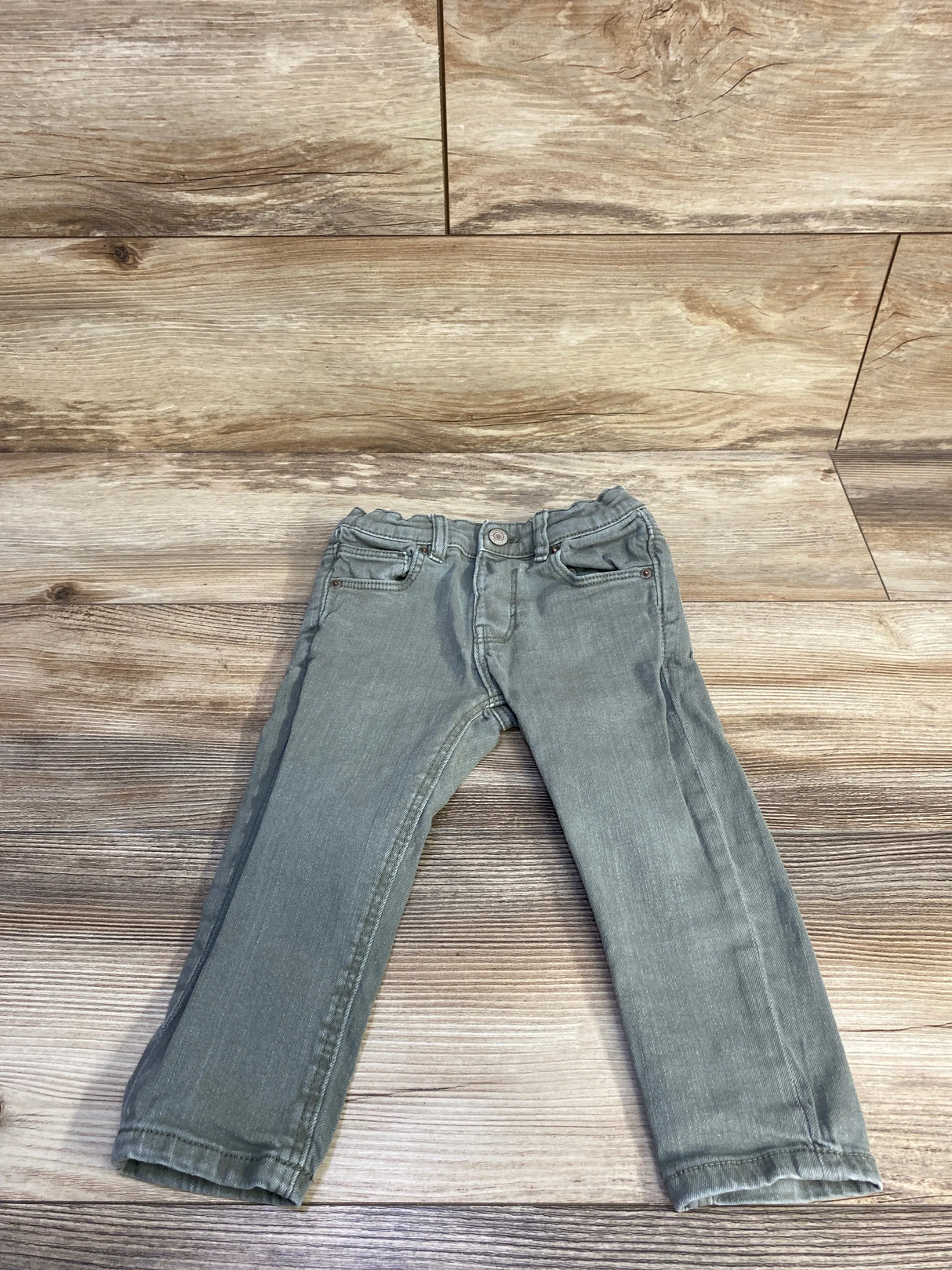 Flat-lay front of toddler green slim denim jeans showing elasticized waist and straight legs on wood background