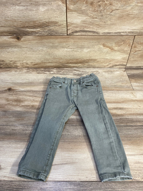 Flat-lay front of toddler green slim denim jeans showing elasticized waist and straight legs on wood background