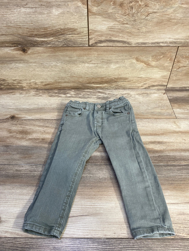 Flat-lay front of toddler green slim denim jeans showing elasticized waist and straight legs on wood background