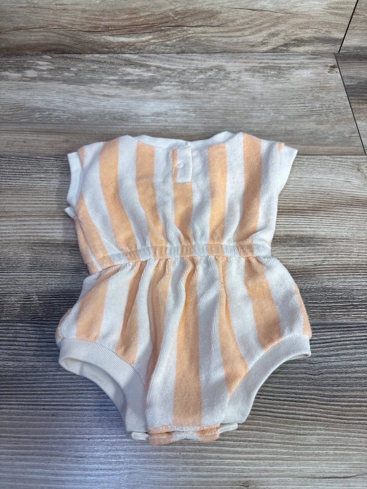 Flat lay of Cat & Jack newborn terry cloth romper with tan and white vertical stripes, elastic waist, and snap crotch on wood background