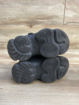 Pair of black kids' sneakers with textured rubber soles on wood surface