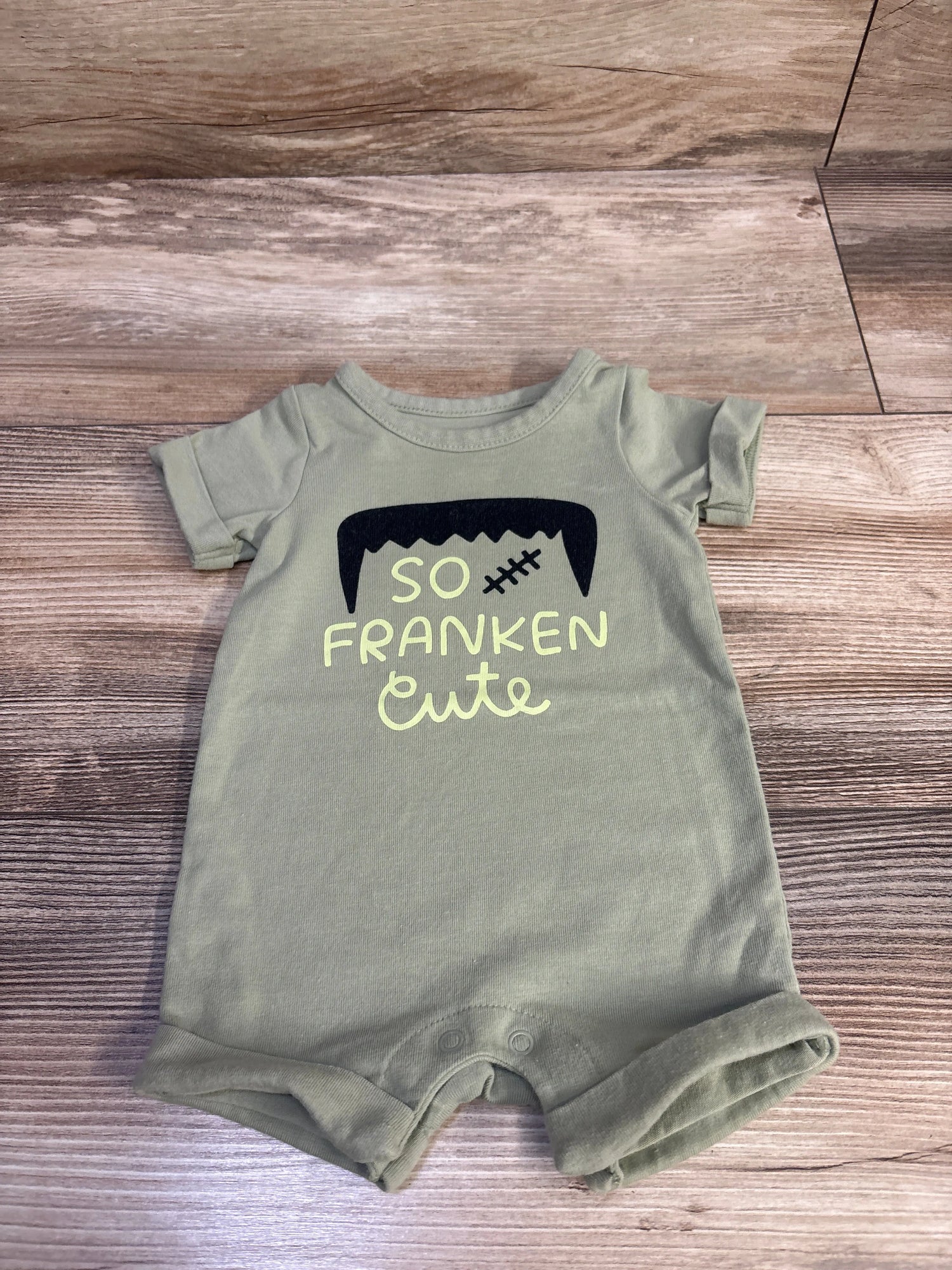 Front view of Cat and Jack So Franken Cute shortie romper showcasing green color, short sleeves, rolled cuffs, and graphic text