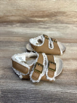 Tan baby sandals with faux fur lining and double buckle straps on wood background