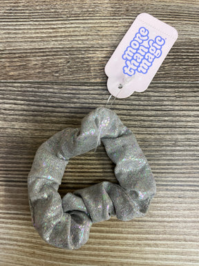 silver holographic fabric scrunchie with More Than Magic tag on wood surface