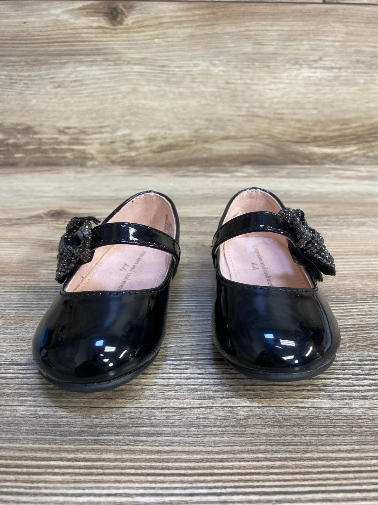Black patent leather girls' dress shoes with bow detail on wood floor