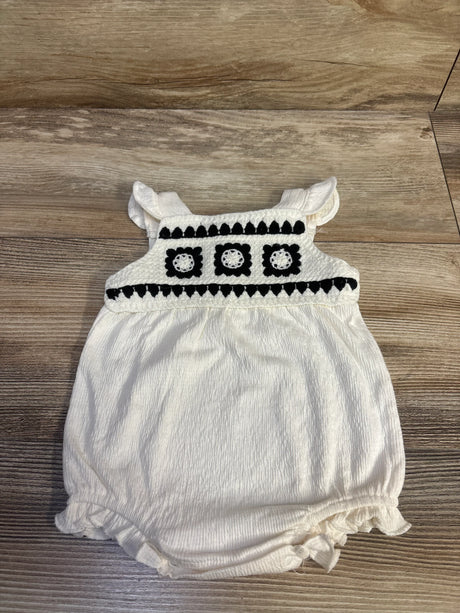 Front of Nicole Miller ivory crochet bubble romper with black crochet yoke, ruffled straps, and elasticized legs on wood