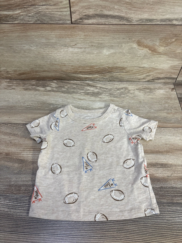 Flat lay of beige baby short-sleeve tee showing all-over football and pennant print on wood floor background