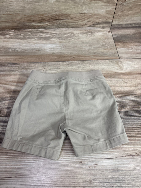 Front view of French Toast drawstring shorts in khaki, size 3T, showcasing an elastic waistband and hem bands on a wood-look floor