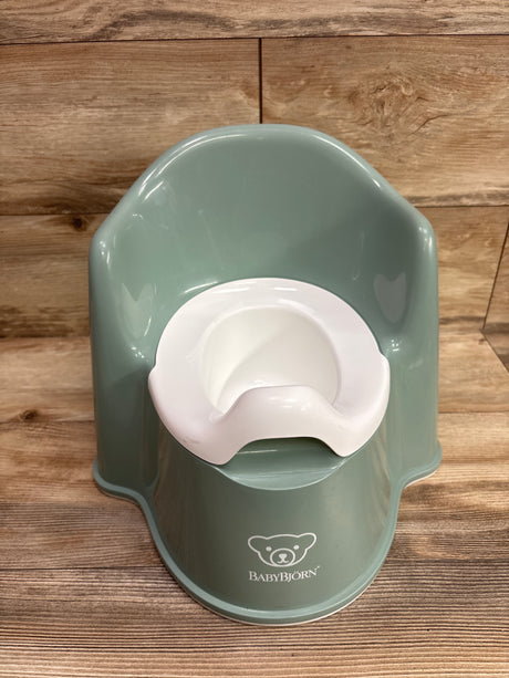 Front view of green BabyBjorn potty chair showcasing white inner bowl and raised back on a wood plank background
