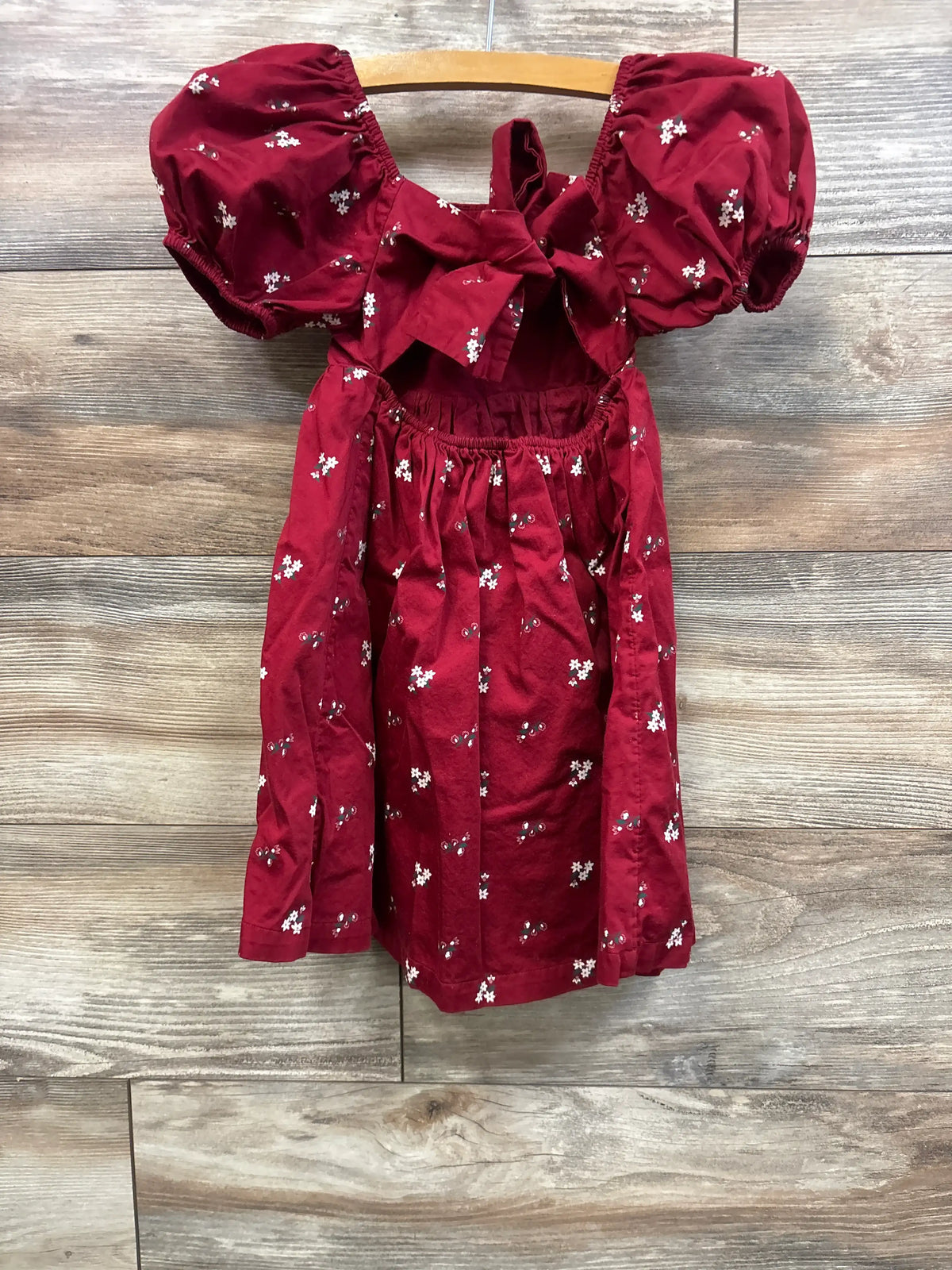 Front view of a Nordstrom red floral puff sleeve dress, size 4T, with a bow neckline against a wood background
