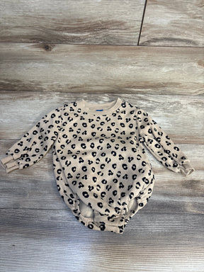 Beige baby onesie with black leopard print, long sleeves, laid on wood floor