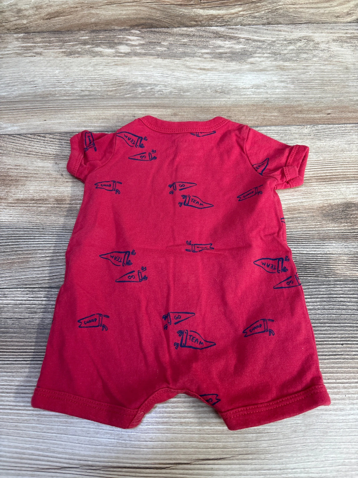 Back view of Carter's newborn shortie romper showing short sleeves and navy pennant print on red fabric, laid flat on wood background