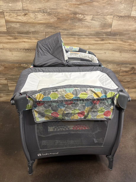 Front view of Baby Trend Lil Snooze Playard Deluxe II with gray frame, Funfetti patterned bassinet and changing pad