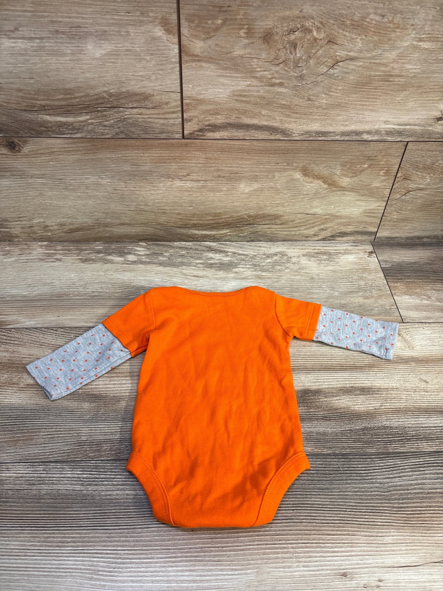 Front view of orange Halloween bodysuit in size 0-3 months showcasing gray sleeves with orange dots on a wood floor