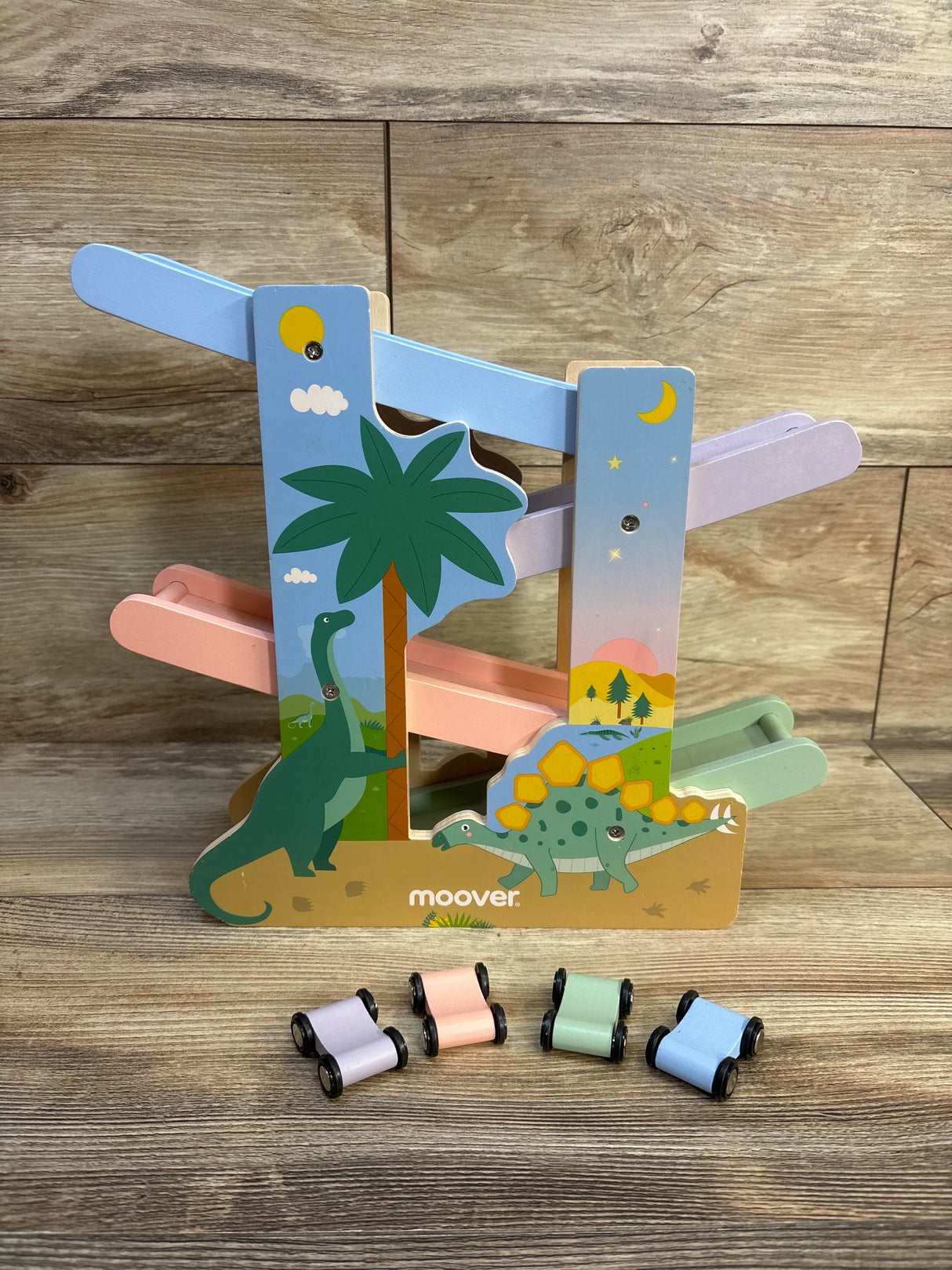 Wooden dinosaur ramp racer toy with pastel tracks and four small pastel cars on wood floor