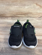 Black Skechers toddler sneakers with green accents and Velcro straps on wood background