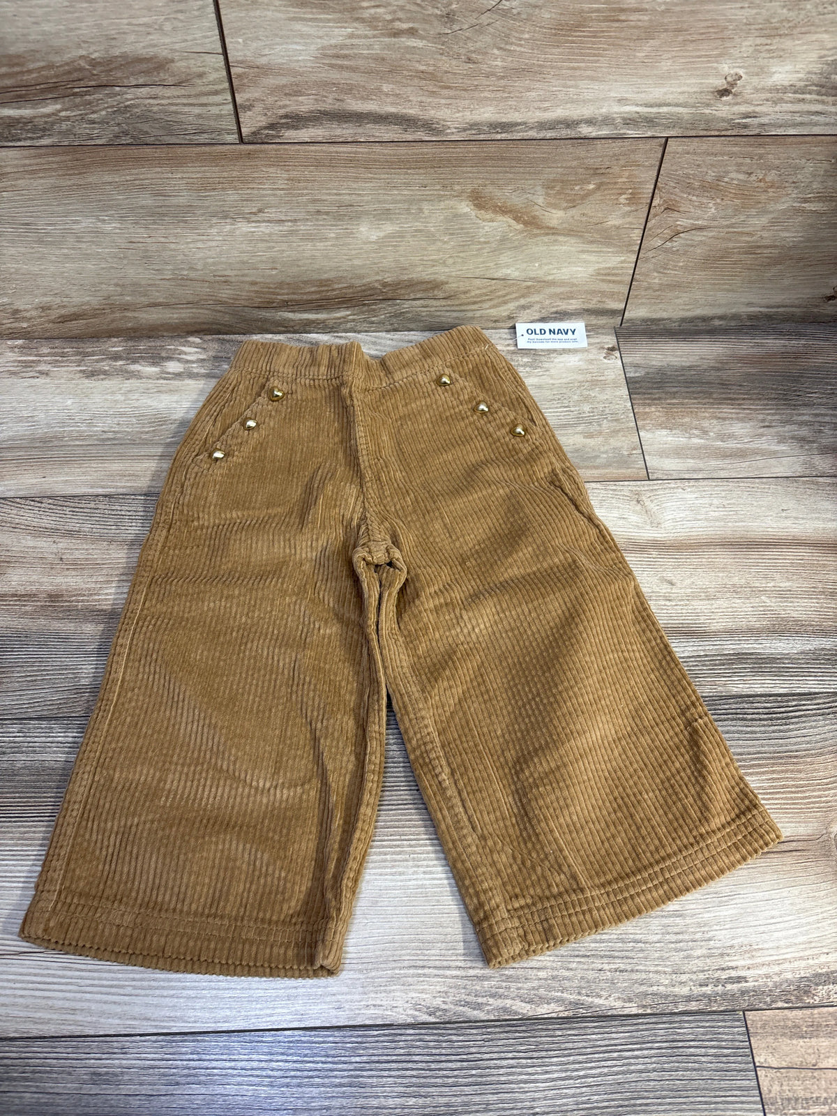 Front view of Old Navy tan wide-leg corduroy pants, toddler size 2T, with six gold-tone buttons on wood flooring