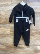 Front view of black Nike toddler hoodie and joggers showing white Nike swoosh and elastic waistband on wooden floor